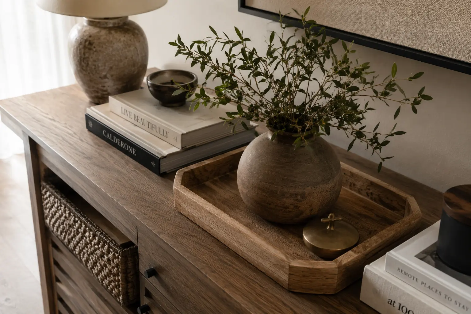 Close-up styled vignette of a console table mixing wood, ceramic, and metal accents