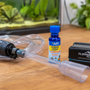 Essential aquarium cleaning tools including a gravel vacuum and water conditioner